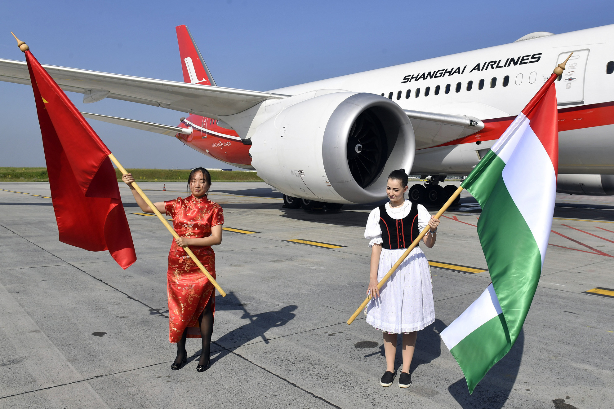 Forrás: MTI/Máthé Zoltán Magyar és kínai zászlóval köszöntik a Shanghai Airlines repülőgépét érkezése napján a Budapest Liszt Ferenc Nemzetközi Repülőtéren