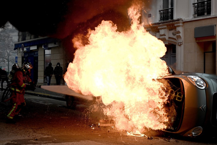Egy tűzoltó próbál eloltani egy égő autót, amit a tüntetők gyújtottak fel