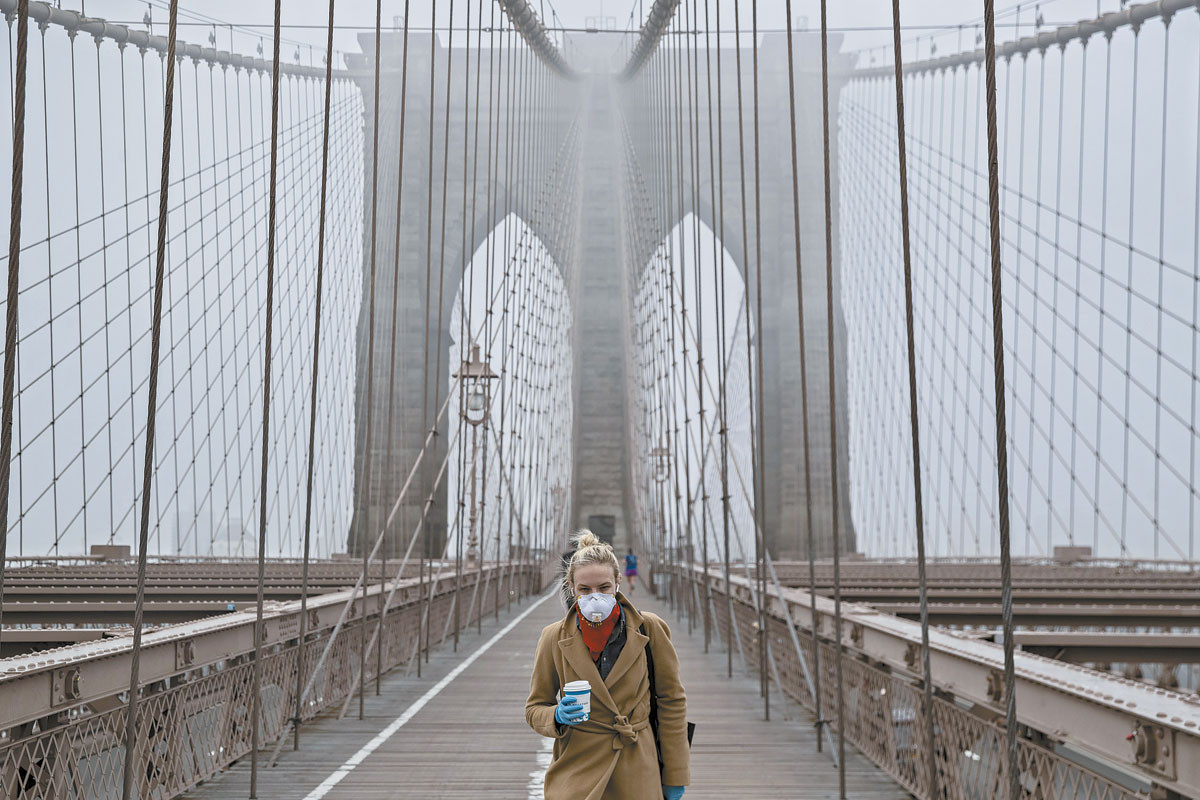 A New York-i Brooklin Bridge-en egy nő, talán munkába igyekszik – ő is egyike lehet azoknak, akiknek „életbevágó” munkaköre miatt engedélyezett a mozgás