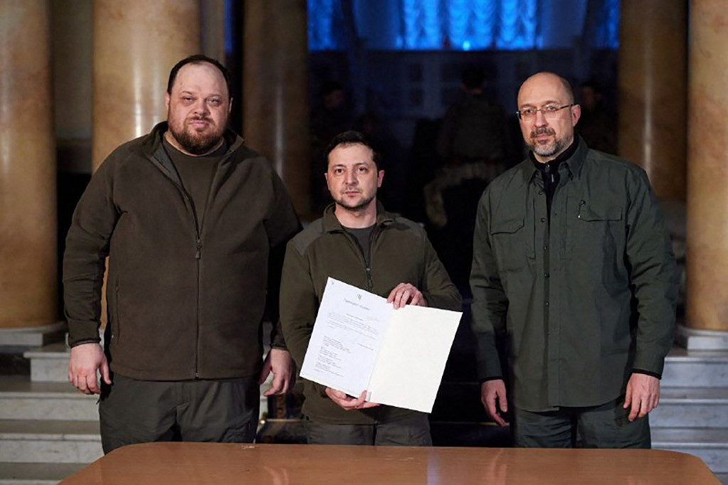 Az aláírás után Volodimir Zelenszkij elnök (középen) mutatja Ukrajna EU-csatlakozási kérelmét. Mellette jobbra Denisz Smihal miniszterelnök, balra Ruszlan Sztefancsuk házelnök