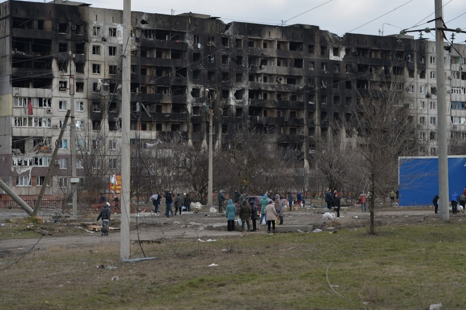 Lakók egy bombatámadás sújtotta épület előtt Mariupolban