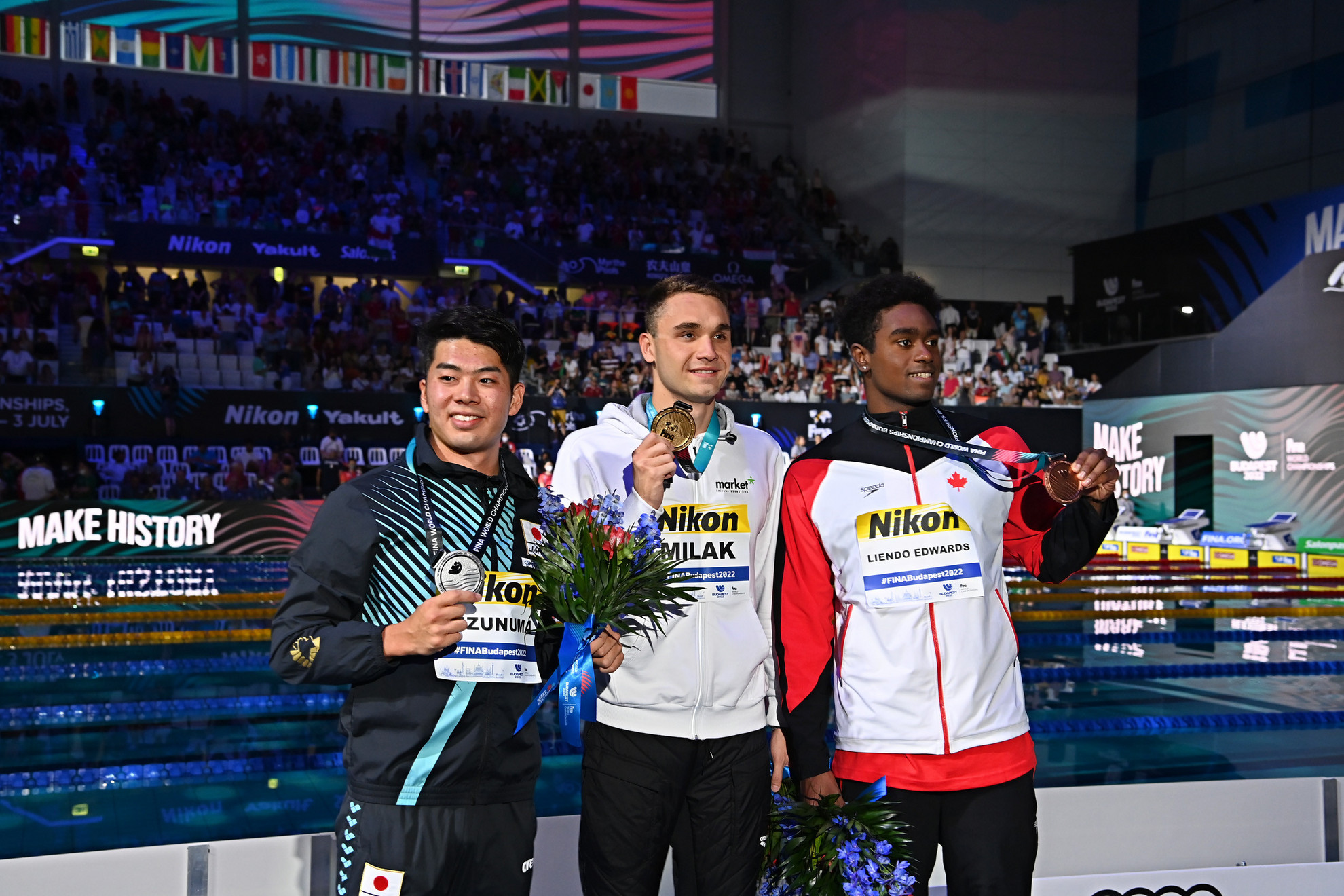 Az aranyérmes Milák Kristóf (k), a második helyezett japán Mizunuma Naoki (b) és a harmadik helyezett kanadai Joshua Liendo Edwards (j) a férfi 100 méteres pillangóúszás eredményhirdetésén a vizes világbajnokságon a Duna Arénában 2022. június 24-én
