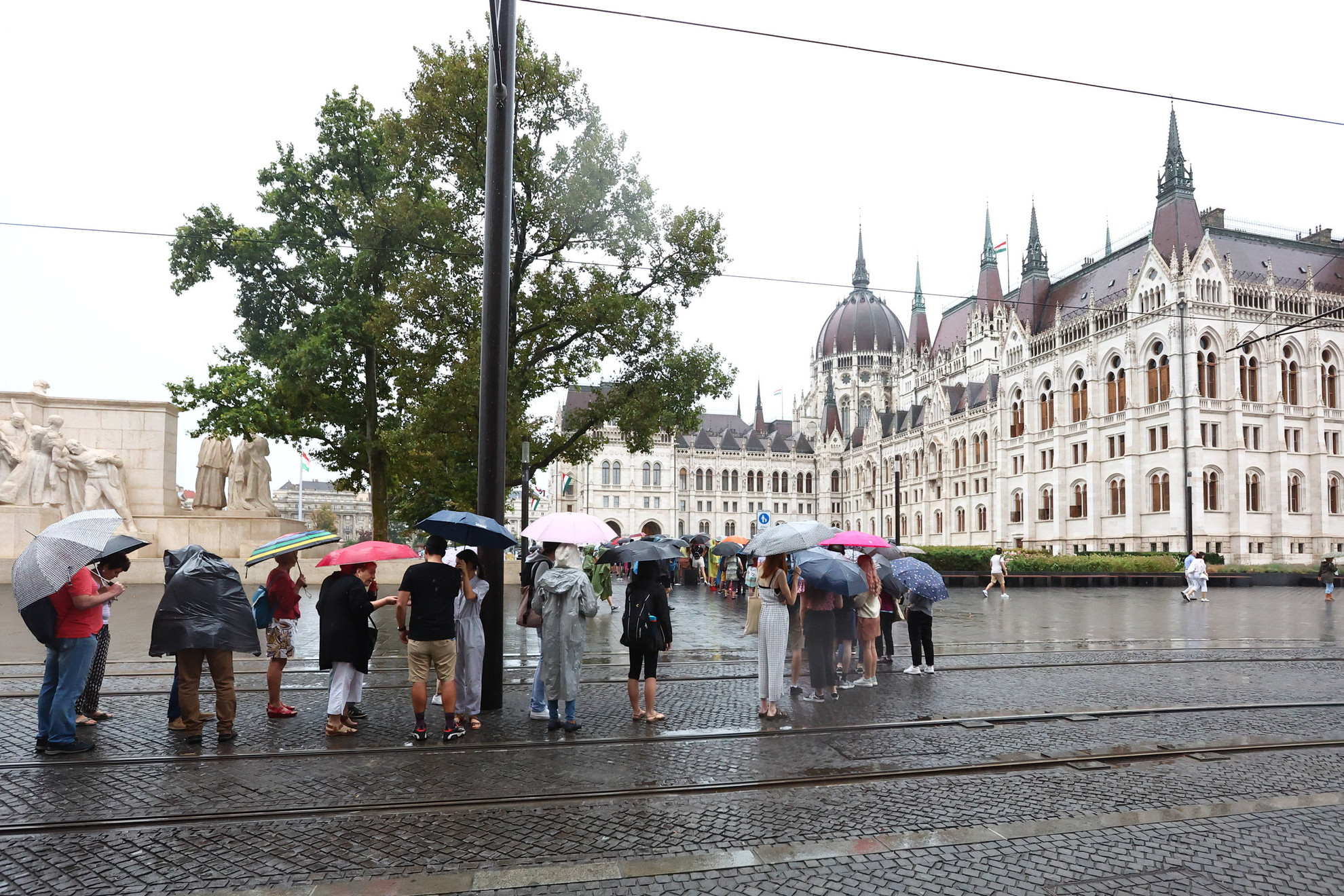 Az augusztus 20-ai nemzeti ünnep alkalmából rendezett nyílt napra érkező látogatók állnak sorban esernyőket tartva az Országház előtt 2022. augusztus 20-án