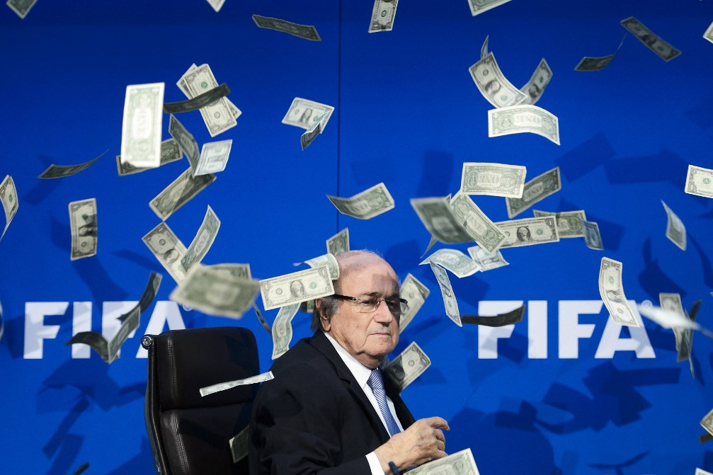 Sepp Blatter, a FIFA akkori elnöke azt nézi, amint körülötte hamis dollárjegyek repkednek, amelyeket egy brit humorista dobott rá a világszervezet zürichi központjában tartott sajtótájékoztatón