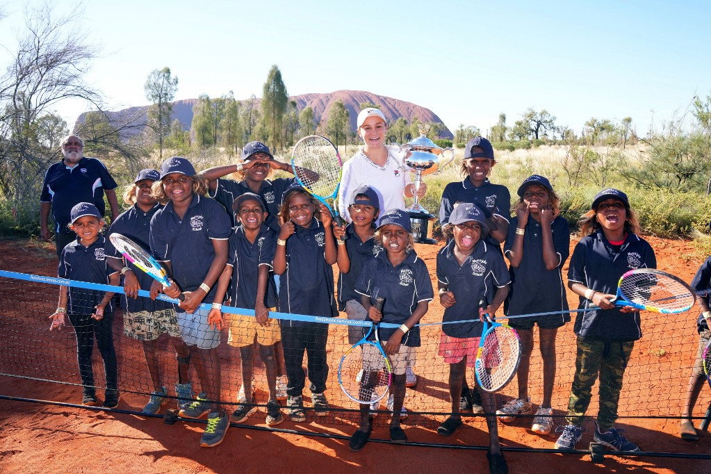Ash Barty 2022-ben az Australian Open serleggel egy csapatnyi aboriginal gyerek társaságában a bennszülöttek földjén, az Ulurunál