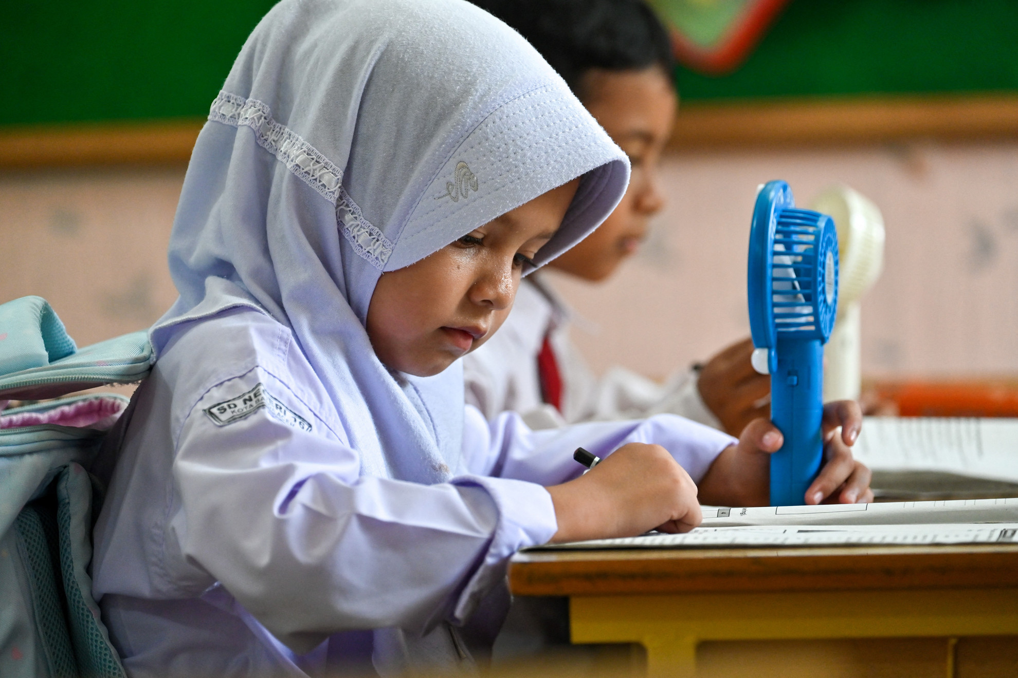 Egy általános iskolás diák egy hordozható ventilátort használ, hogy hűtse magát az osztályteremben a forróságban Banda Acehben, Indonéziában 2023. május 15-én.