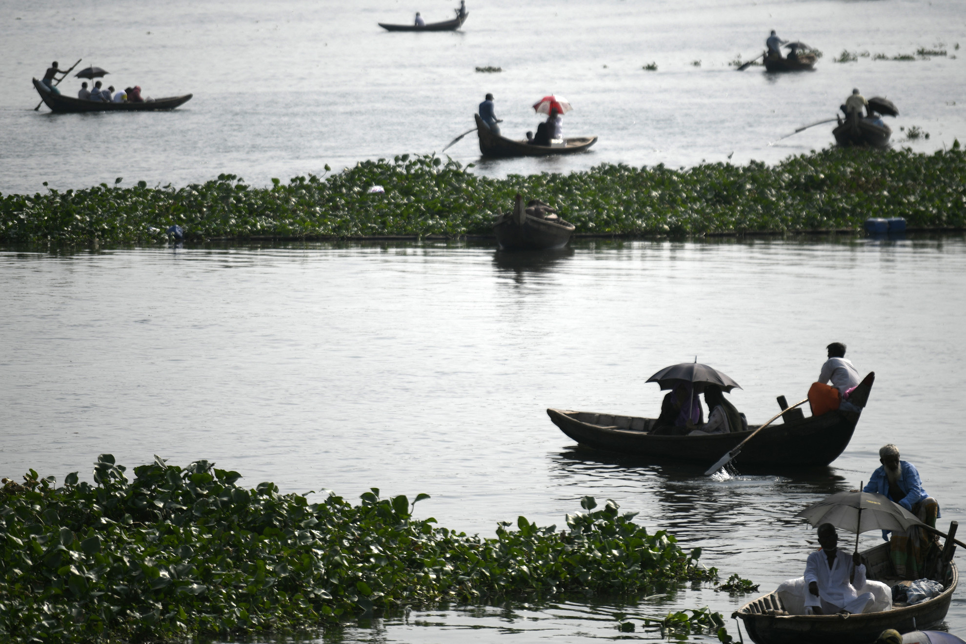 Utasok kelnek át a Buriganga folyón, miközben ernyőt tartanak, hogy megóvják magukat a forró napsütéstől a bangladesi Dakkában, 2023. május 06-án. Az uralkodó mérsékelt, hőhullámos állapot a bangladesi meteorológiai hivatal (BMD) szerint valószínűleg a következő napokban is folytatódik az országban.