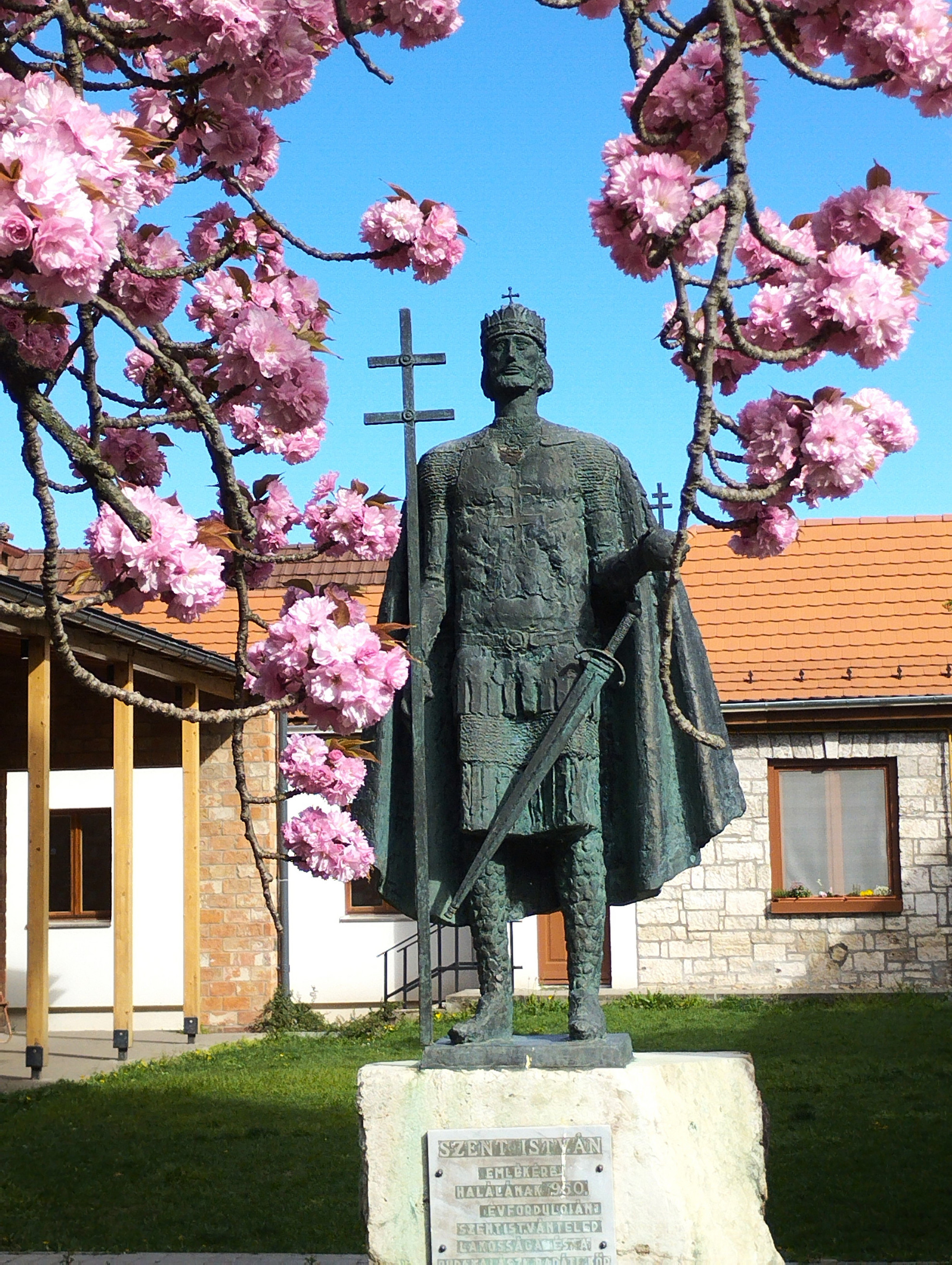 Virágkoszorúban Szent István szobra a templom kertben