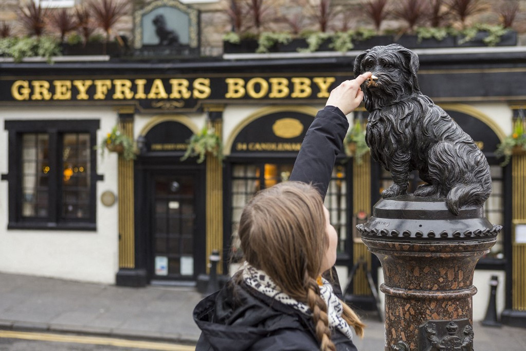 Egyesült Királyság, Skócia, Edinburgh, a Világörökség része, egy turista megérinti Bobby orrát a Greyfriars Bobby bárja előtt